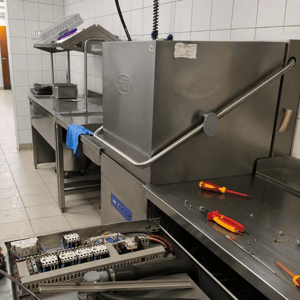 Servis profesionalne mašine za pranje posuđa u ugostiteljskoj kuhinji: otvoren električni ormarić i alat na inox radnoj ploči